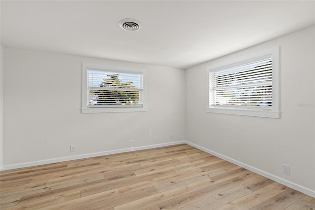 unfurnished room with light wood finished floors, plenty of natural light, visible vents, and baseboards