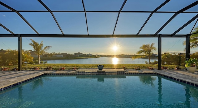 pool at dusk with a lanai, a patio area, and a water view