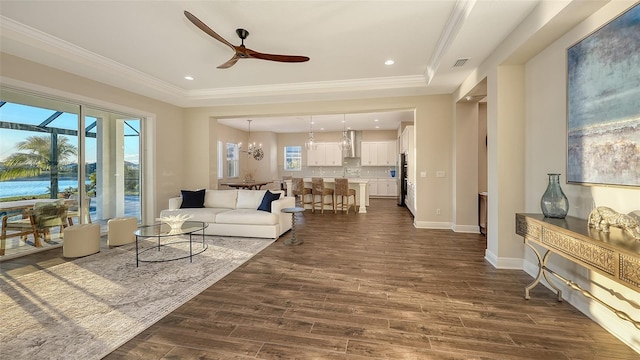 living room featuring crown molding, a tray ceiling, dark hardwood / wood-style floors, and ceiling fan with notable chandelier