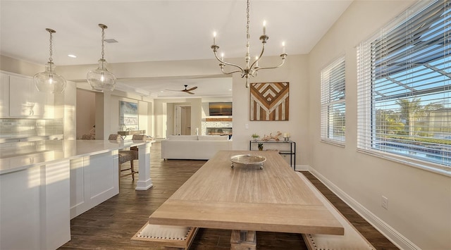 dining area featuring a fireplace, ceiling fan with notable chandelier, and dark wood-type flooring