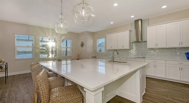 kitchen with pendant lighting, sink, an island with sink, and wall chimney exhaust hood