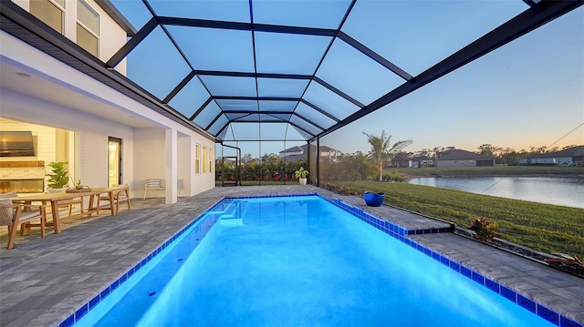 pool at dusk with a water view, a patio area, and glass enclosure