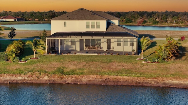 back house at dusk with a yard, a patio area, and a water view