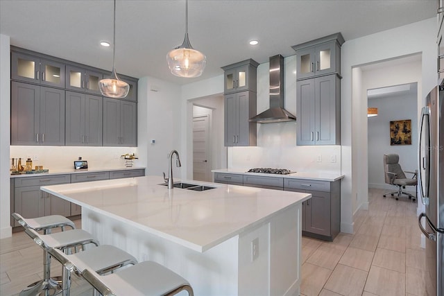 kitchen with hanging light fixtures, a kitchen island with sink, wall chimney range hood, and a kitchen bar