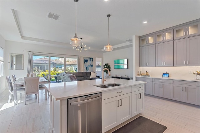 kitchen with sink, a kitchen island with sink, decorative light fixtures, stainless steel dishwasher, and a raised ceiling