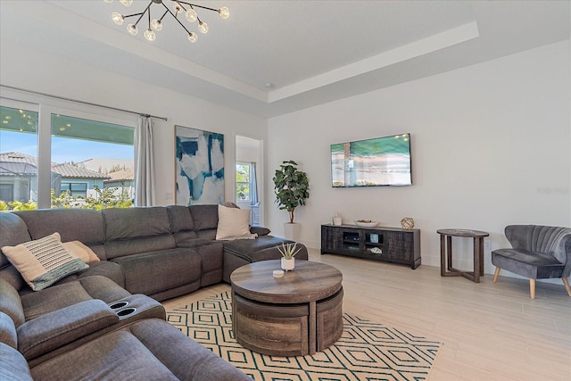 living room featuring an inviting chandelier, a tray ceiling, and light hardwood / wood-style floors