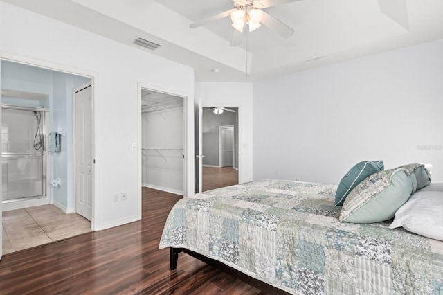 bedroom featuring wood-type flooring, a spacious closet, a raised ceiling, a closet, and ceiling fan