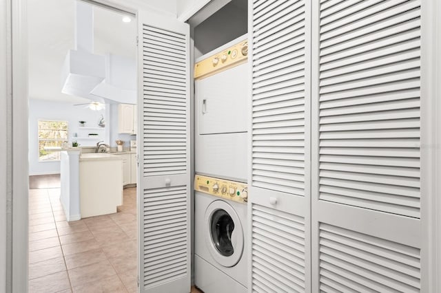 laundry area featuring stacked washer / dryer, light tile patterned floors, and ceiling fan