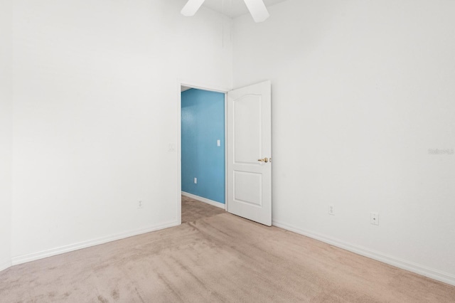 unfurnished room with ceiling fan, light colored carpet, and a towering ceiling