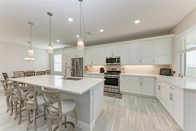 kitchen with appliances with stainless steel finishes, white cabinetry, sink, a kitchen bar, and hanging light fixtures