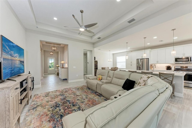 living room with a raised ceiling and ceiling fan