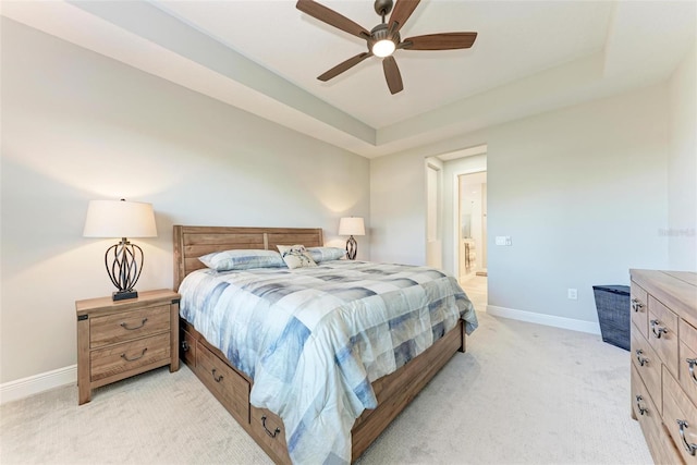 bedroom with ensuite bathroom, light colored carpet, ceiling fan, and a tray ceiling