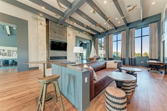 living room featuring a large fireplace, beam ceiling, light hardwood / wood-style floors, and a high ceiling