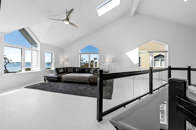 living room with ceiling fan, tile patterned flooring, a skylight, a water view, and beamed ceiling