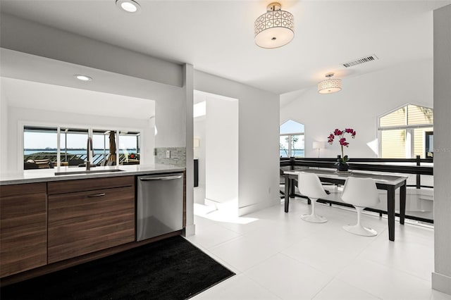 kitchen with stainless steel dishwasher, dark brown cabinets, sink, and decorative backsplash