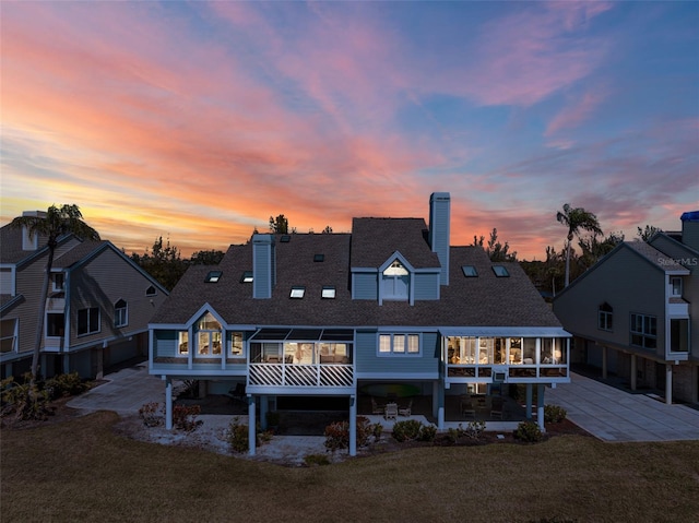 back house at dusk featuring a lawn and a patio area