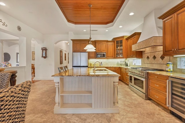 kitchen with wine cooler, sink, a center island with sink, a raised ceiling, and stainless steel appliances