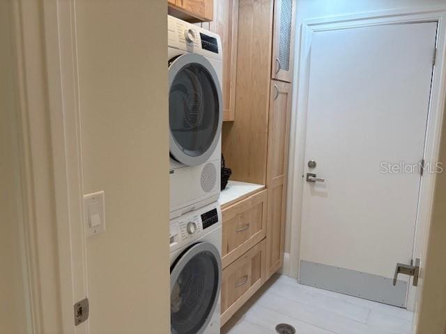 clothes washing area featuring cabinets and stacked washing maching and dryer