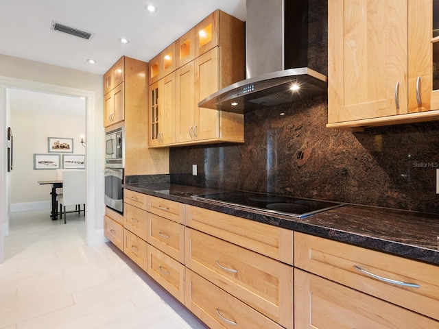 kitchen featuring wall chimney range hood, dark stone countertops, stainless steel appliances, tasteful backsplash, and light brown cabinets