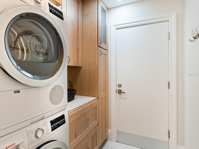 clothes washing area featuring cabinets and stacked washer / dryer