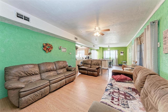 living room with ceiling fan, a textured ceiling, and light hardwood / wood-style floors