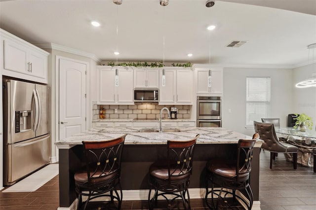 kitchen featuring stainless steel appliances, white cabinetry, hanging light fixtures, and a kitchen island with sink