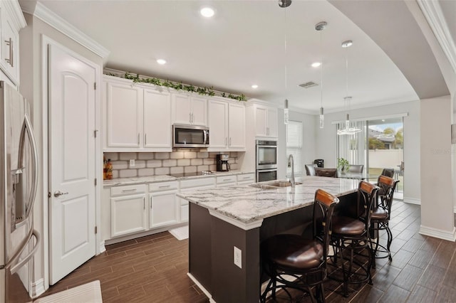 kitchen with sink, hanging light fixtures, stainless steel appliances, a kitchen island with sink, and white cabinets