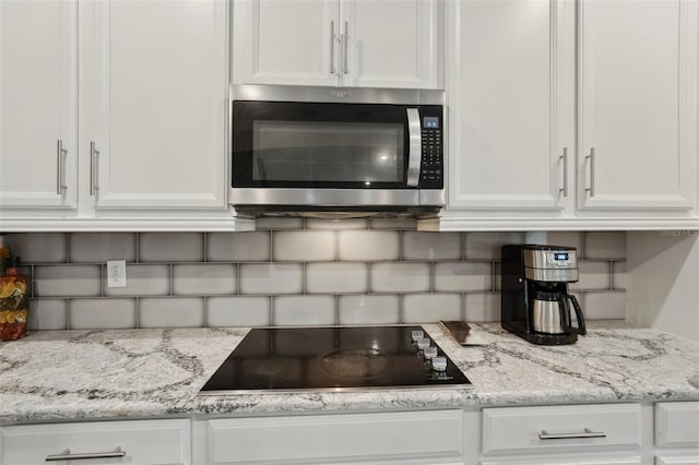 kitchen featuring black electric cooktop, white cabinetry, light stone counters, and tasteful backsplash