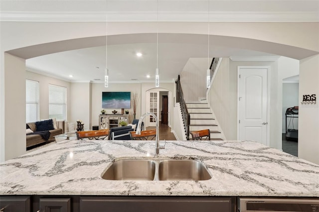 kitchen featuring pendant lighting, crown molding, light stone countertops, and sink