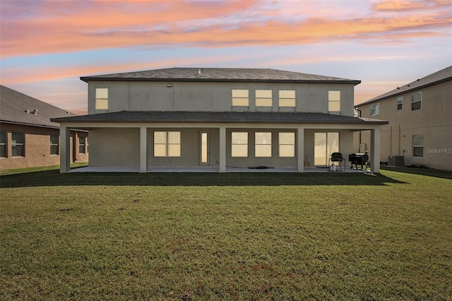 back house at dusk featuring central AC unit, a yard, and a patio area