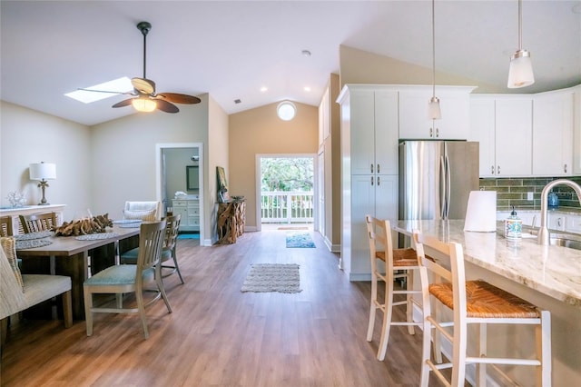 kitchen with hardwood / wood-style flooring, stainless steel refrigerator, backsplash, light stone countertops, and white cabinets