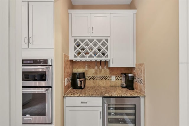 bar with white cabinetry, backsplash, beverage cooler, and stainless steel double oven