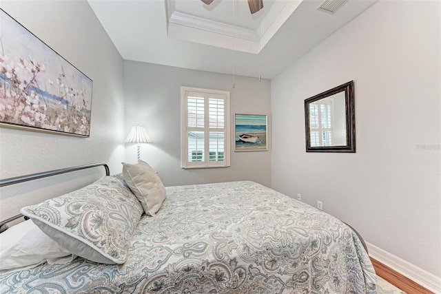 bedroom featuring hardwood / wood-style flooring, ornamental molding, a raised ceiling, and ceiling fan