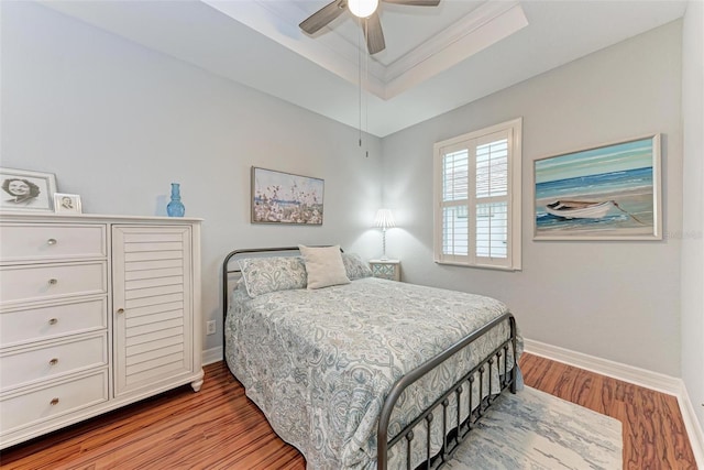 bedroom with crown molding, hardwood / wood-style floors, ceiling fan, and a tray ceiling