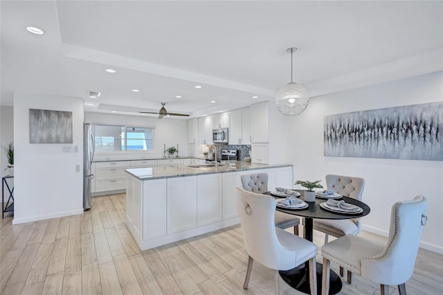 kitchen with appliances with stainless steel finishes, white cabinetry, hanging light fixtures, light stone countertops, and light hardwood / wood-style flooring