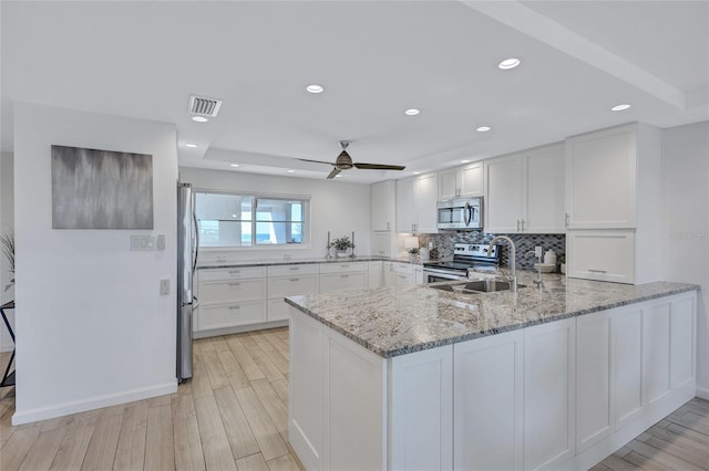 kitchen with white cabinetry, tasteful backsplash, light stone counters, kitchen peninsula, and stainless steel appliances