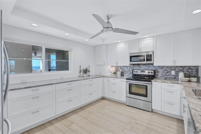 kitchen featuring white cabinetry, light stone counters, tasteful backsplash, light wood-type flooring, and stainless steel appliances