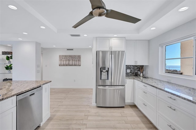 kitchen with stainless steel appliances, a tray ceiling, light stone countertops, and white cabinets