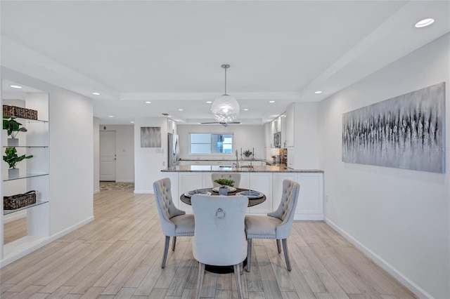 dining room with a tray ceiling, sink, and light hardwood / wood-style flooring