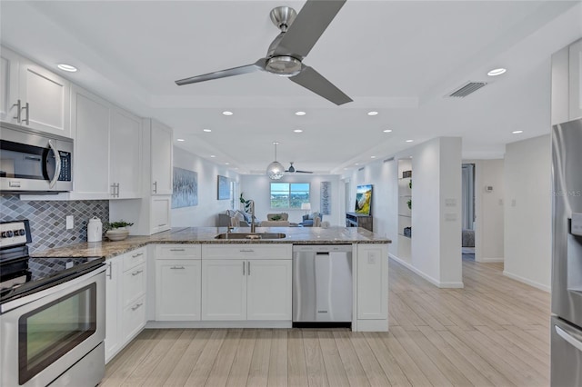 kitchen featuring appliances with stainless steel finishes, white cabinets, light stone counters, and kitchen peninsula