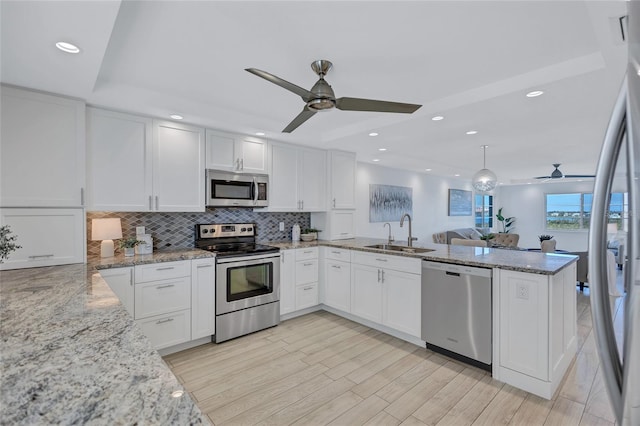 kitchen featuring stainless steel appliances, kitchen peninsula, sink, and white cabinets