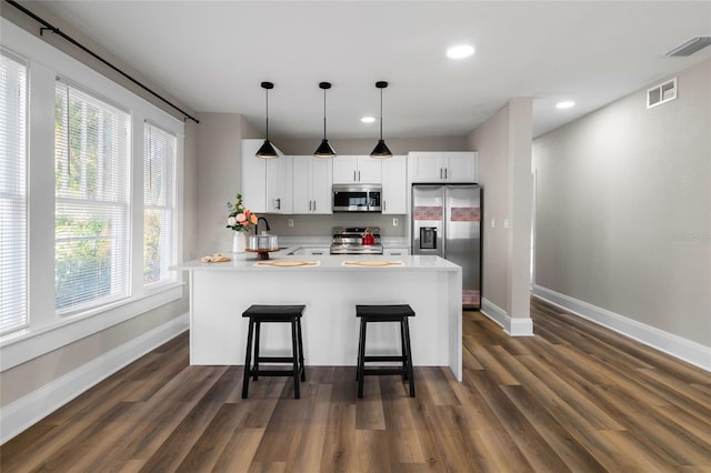 kitchen featuring appliances with stainless steel finishes, a breakfast bar, decorative light fixtures, sink, and white cabinets