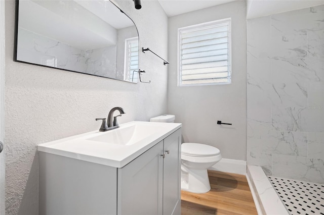 bathroom featuring hardwood / wood-style flooring, tiled shower, vanity, and toilet