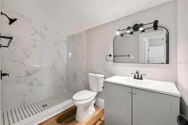 bathroom with wood-type flooring, a tile shower, vanity, and toilet