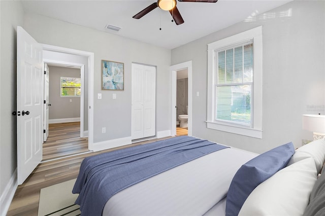 bedroom with ensuite bath, dark wood-type flooring, ceiling fan, and a closet