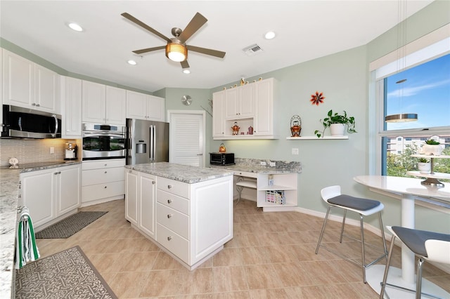 kitchen featuring white cabinetry, light stone counters, stainless steel appliances, and a center island