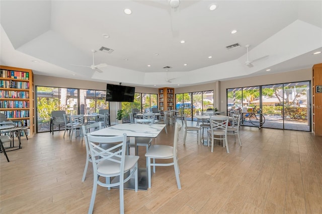 dining space with ceiling fan, a tray ceiling, and light hardwood / wood-style floors