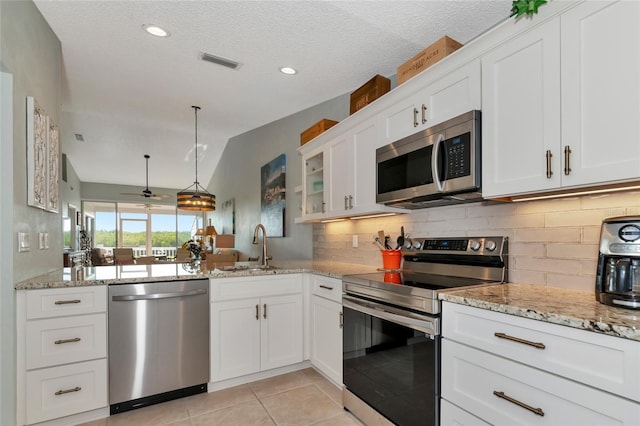 kitchen featuring lofted ceiling, sink, appliances with stainless steel finishes, white cabinets, and decorative light fixtures