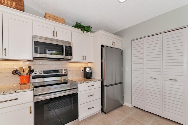 kitchen with appliances with stainless steel finishes, white cabinetry, light stone counters, light tile patterned flooring, and decorative backsplash