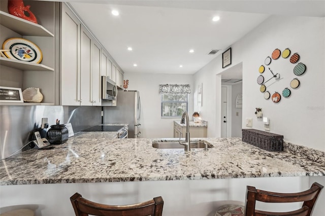 kitchen featuring light stone counters, appliances with stainless steel finishes, a breakfast bar, and sink